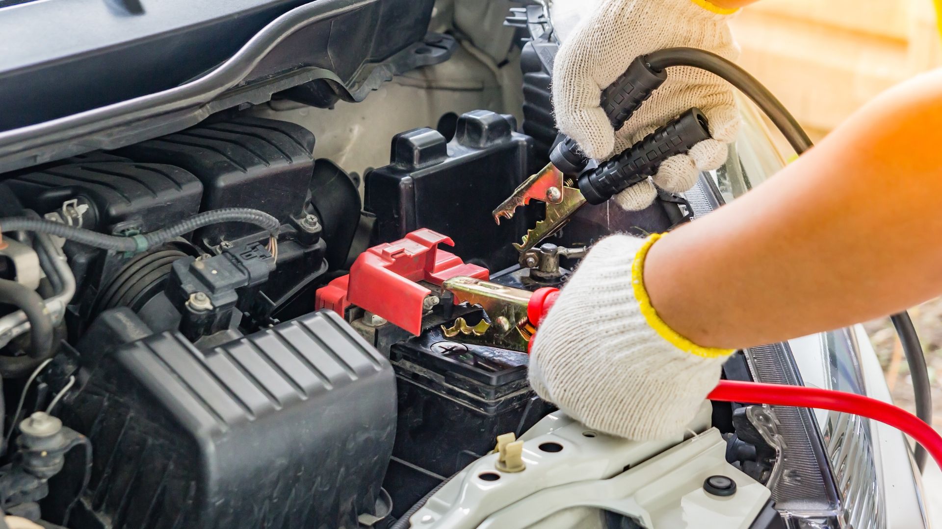 Mechanic's gloved hand connecting jumper cables to car battery