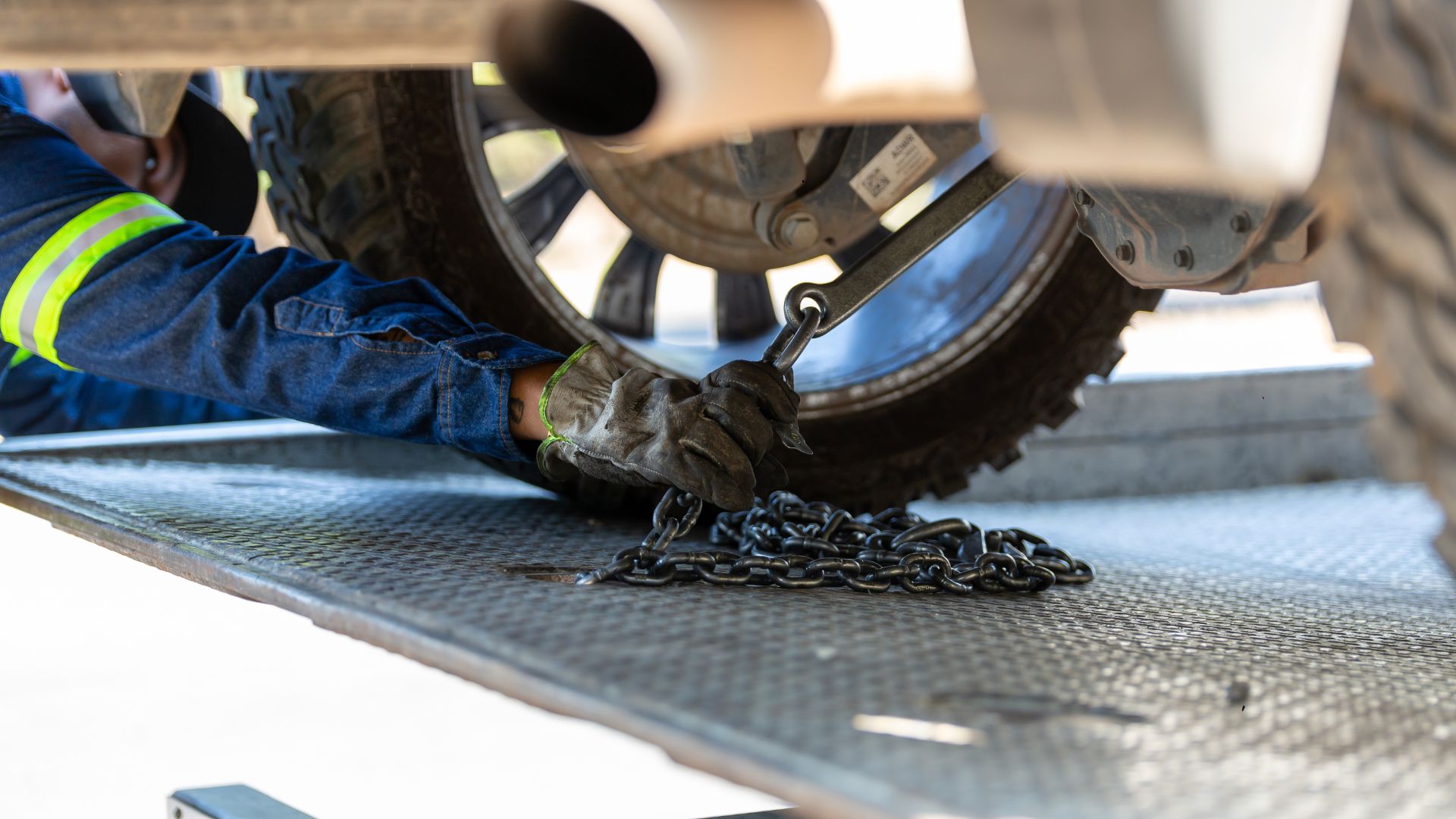Worker in safety gear securing chain near vehicle tire on metal platform