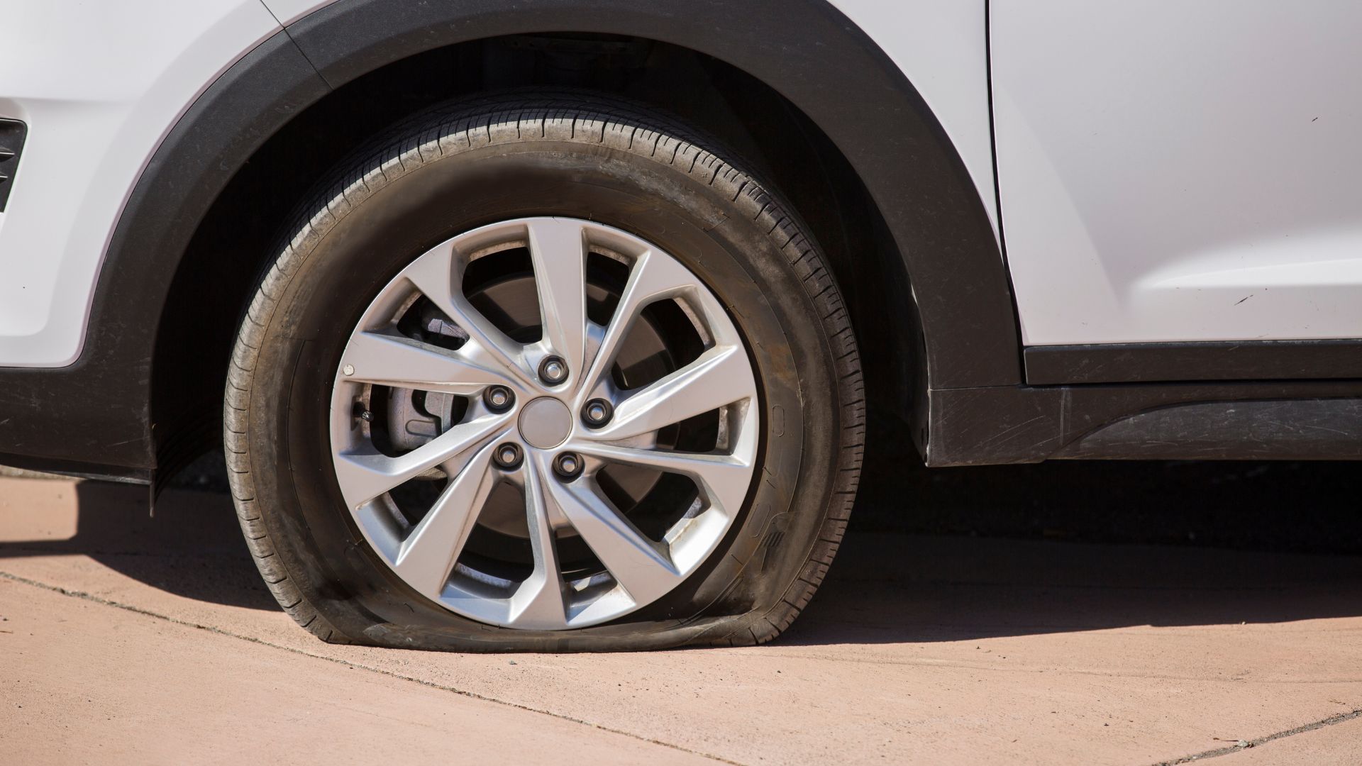 Flat tire on white car with silver wheel, deflated on concrete surface