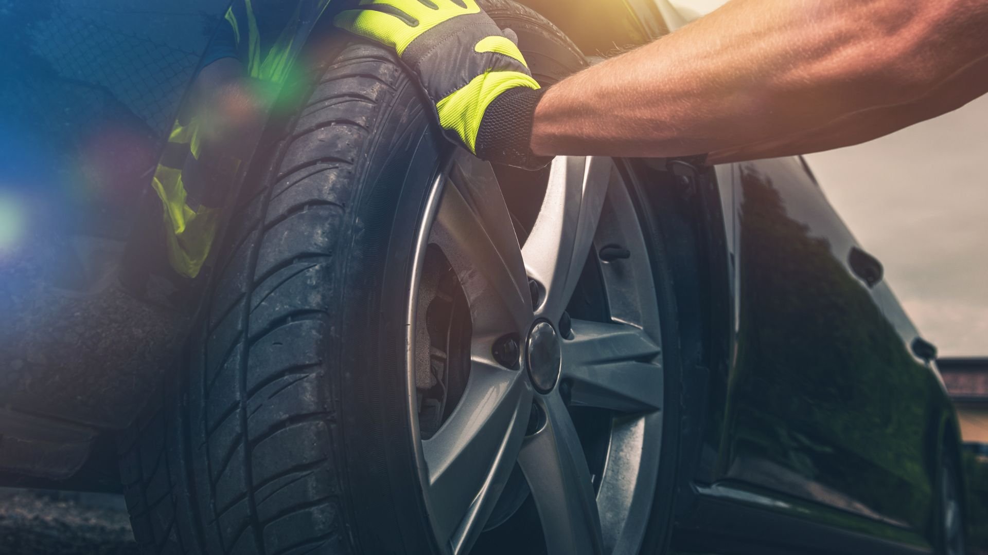 Mechanic's hands checking car tire tread with yellow-gloved grip